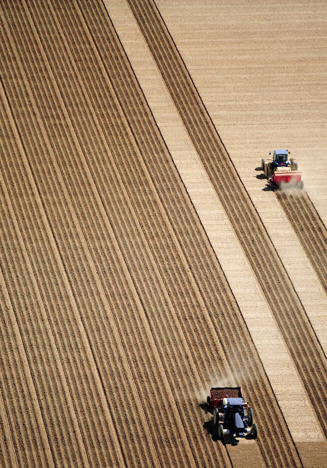 aerial view of 2 tractors planting potatoes in the fertile farm fields of Idaho, during the spring.