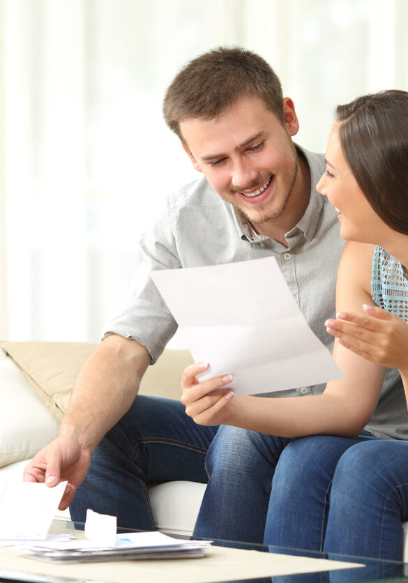 Happy couple reading mail and checking accountancy looking each other sitting on a couch at home