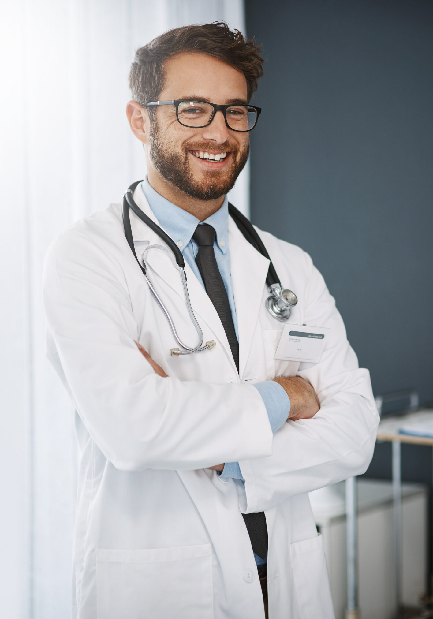 Cropped portrait of a confident young male doctor standing with his arms folded inside of a hospital